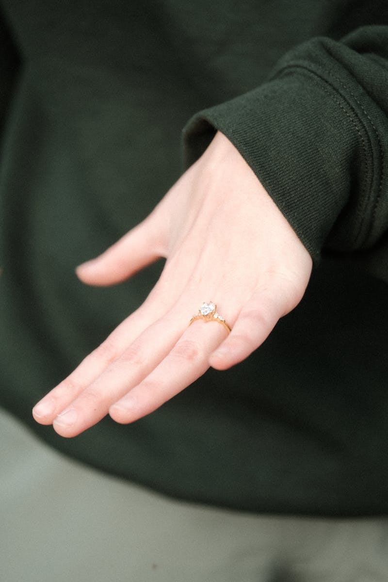 Close-up of a hand wearing an elegant engagement ring, set against a dark green background.